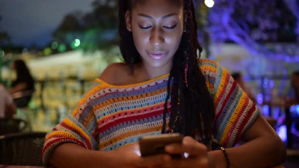 Black woman browsing smartphone in city at night