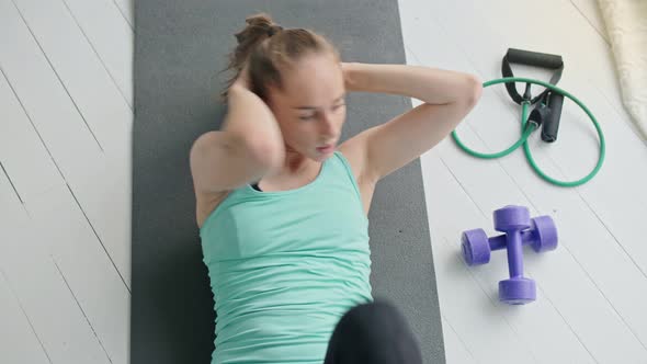 Top View of an Attractive Young Girl Working Out, Doing Exercises for Abs on the Fitness Mat at Home