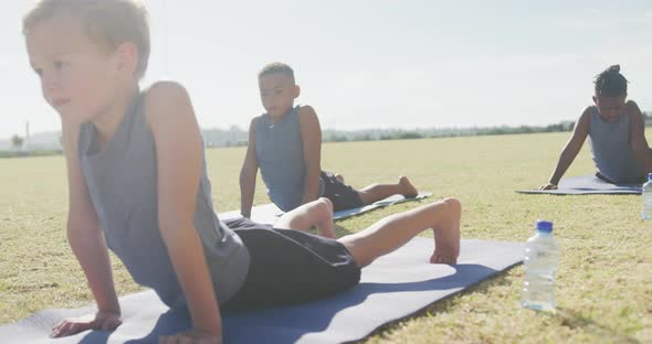 Video of focused diverse boys practicing yoga on mats on sunny day