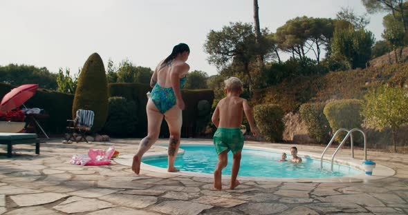 Young woman running with children and jumping into the swimming pool