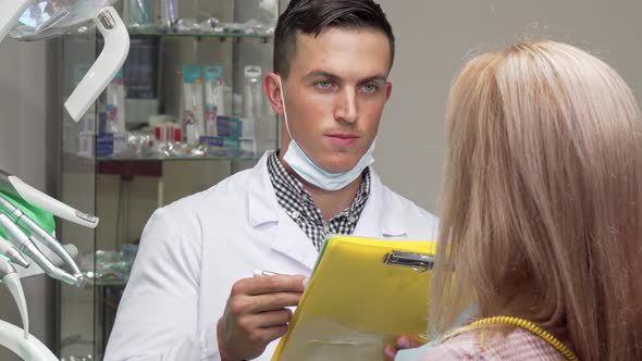 Young Male Dentist Talking To His Female Patient, Examining Medical Papers