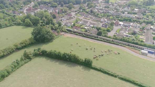 Sideways tracking aerial from right to left of the village of Washford with a diesel train leaving t