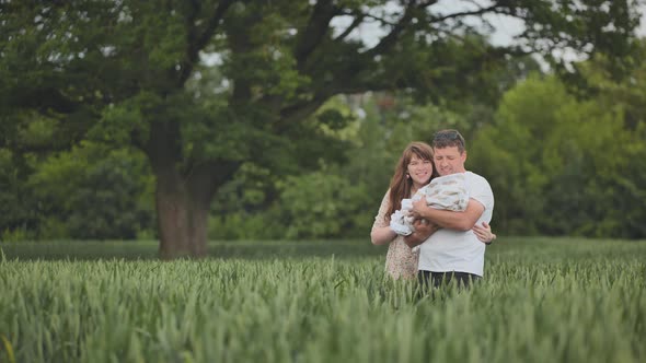 A Young Couple Standing in a Field Kissing and Holding Their Newborn Baby in Their Arms