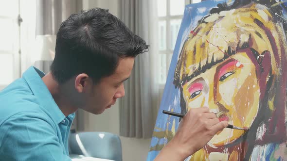 Close Up Side View Of An Asian Artist Man Painting A Girl's Face On The Canvas