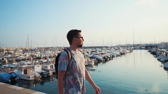 Happy Young Man Is Walking Alone on Pier with Moored Yachts in Summer Day