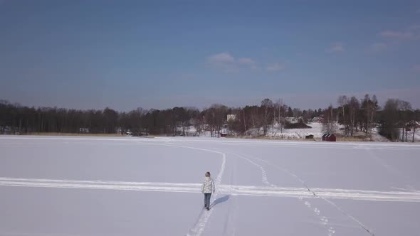 Overhead follow footage of lonesome blonde girl slowly walking on frozen lake on a crisp winter's da