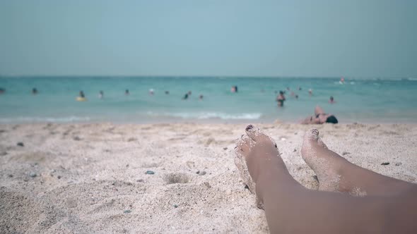 Close Feet of Woman Sunbathing Against Swimming People