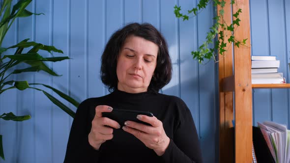 Smiling Middle Age Woman Playing Mobile Game on Smartphone at Home