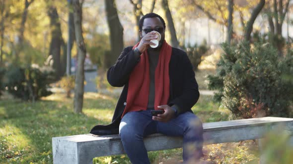 Happy African man drinking coffee in park