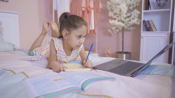 Little girl doing homework on laptop. alt