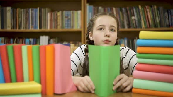 A Schoolgirl Is Hiding Behind a Book in the Library