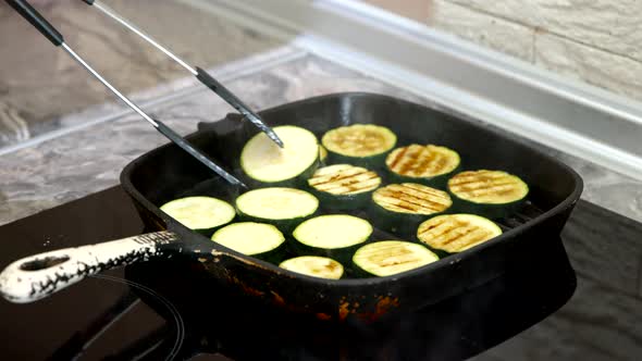 Cook Grills Zucchini on Grill Pan and Turns Them Over with Tongs