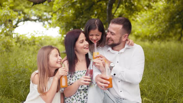 Happy Young Family with Two Children Drinking Fresh Juice While Sitting on