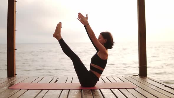 Woman Practicing Yoga Sitting on Mat on Sea Pier Performing Ubhaya Padangusthasana