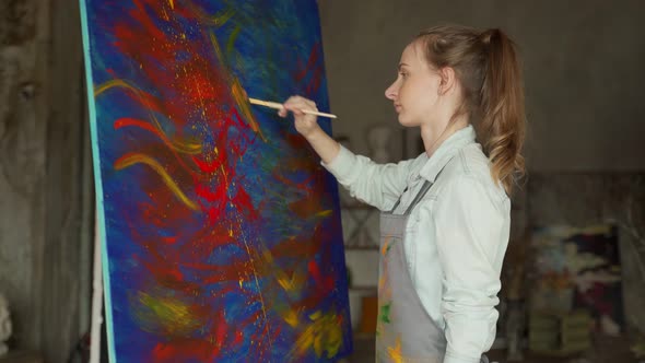 Female Artist in Front of an Easel Painting with a Brush Using Oil or Acrylic Paint