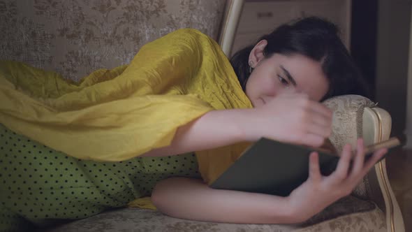 Girl Student Reading a Book in the Evening Lying on the Couch