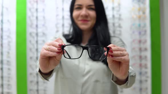 Young Woman Trying on Glasses on the Background of a Shop Window with Spectacle Frames