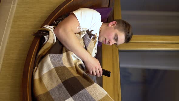 A Young Man Is Texting on the Phone. A Man Lies on a Window Sill By the Window with a Smartphone in