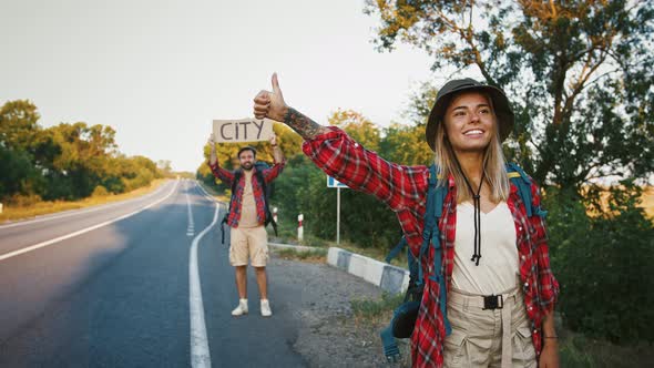 Young Millennial Woman Hitchhiking on Road with Boyfriend Who Holding Sing City