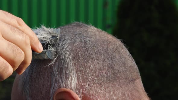 Cutting gray hair on the head of an elderly balding man with a cordless electric machine