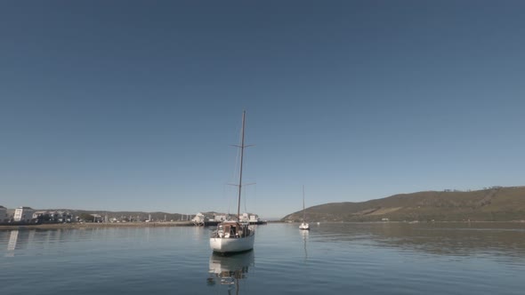 Boat slowly cruises by sailboats moored in Knysna Lagoon on clear day