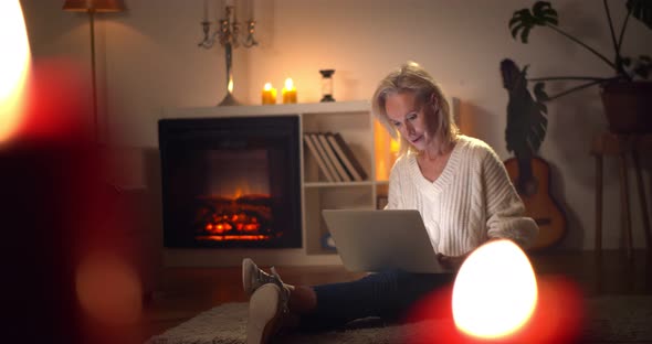 Mature Woman Working on Laptop at Home Sitting Near Fireplace