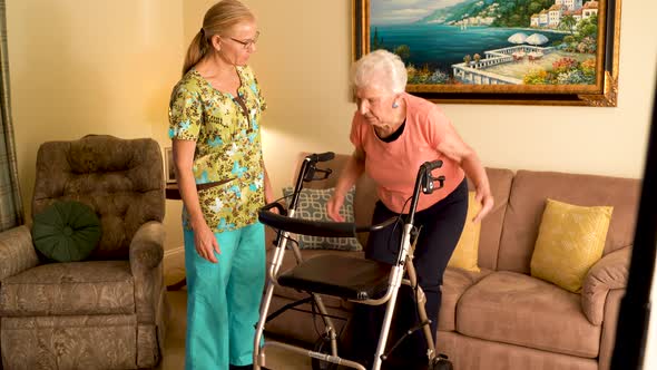 Closeup of home healthcare nurse helps elderly woman get up from couch and use a walker.