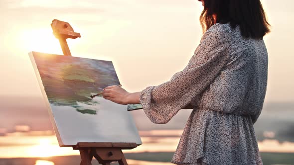 A Young Woman Artist Standing at Sunset and Drawing a Painting of Nature