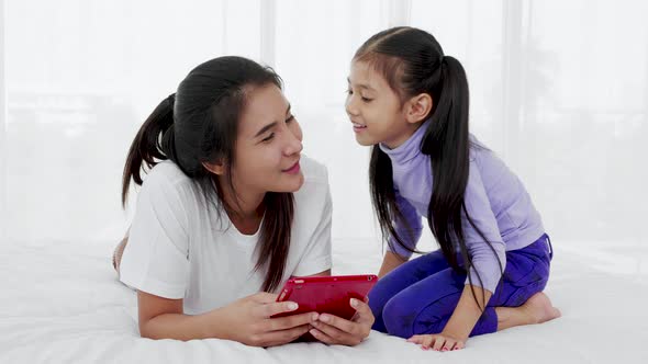 daughter kisses her mother while use tablet on bed, happy single mom concept