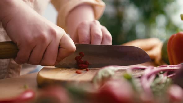 Woman cutting chili peppers on wooden board