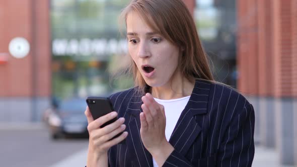 Business Woman in Shock Reacting to Results on Smartphone