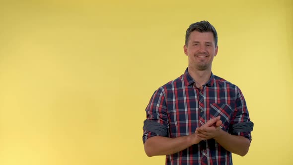 Portrait of Smiling Young Man Giving Applause To Somebody on Yellow Background.