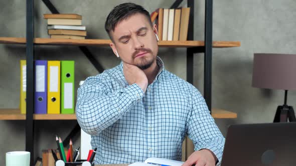 Tired businessman writes in notebook massaging neck after over work at laptop