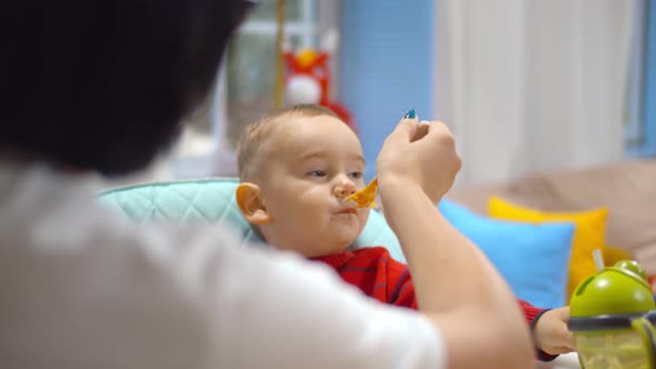 Close Up of Mom Giving Healthy Food To Her Son on High Chair.