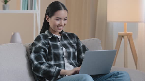 Smiling Asian Woman Happy Student Girl Freelancer Sitting on Couch Using Laptop Typing Message Email