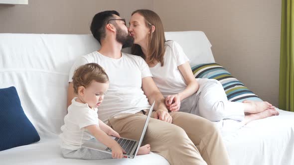 Cheerful Attractive Couple Sitting on the Sofa, Laughing, Looking at Their Baby