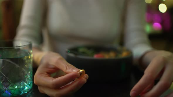 Young Woman Eats Medicine and Drinks with a Glass of Water Before Dinner in a Restaurant