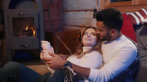 Happy Young Couple Relaxing in Cozy Home Near the Fireplace and Reading a Book Together