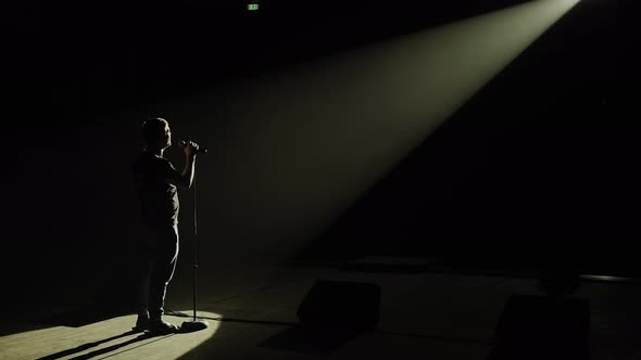 Silhouette of a Man on Stage in the Dark with a Microphone