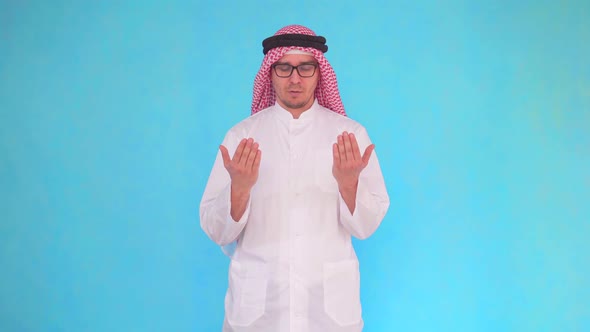 Arab Man Stands on a Blue Background and Turns To God Reading a Prayer