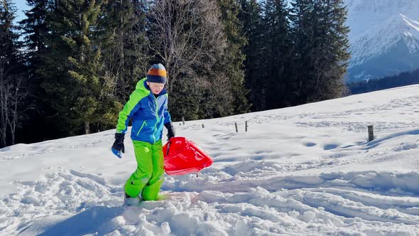 Boy Walk on Uphill with the Sled View Over Mountain Peaks