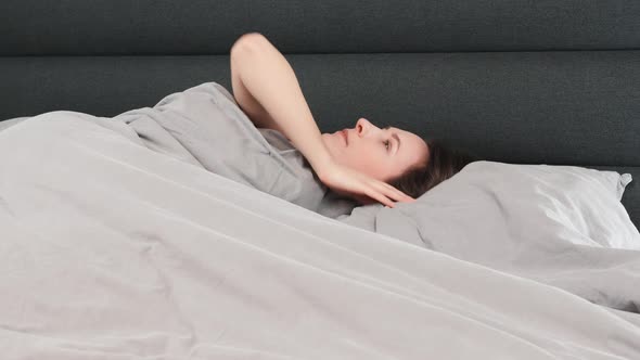 Woman wakes up in the morning on grey bed at home.