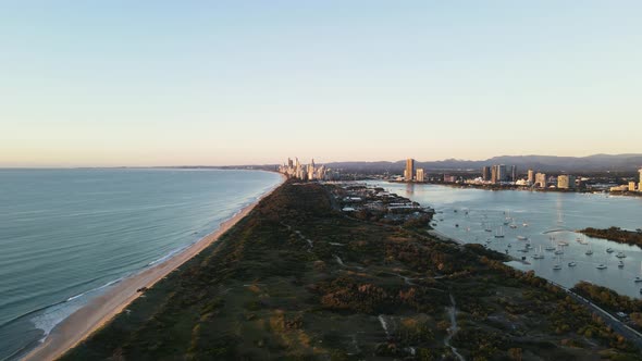 Coastal nature parklands dividing a boat harbor and coastline with an urban city skyline rising abov