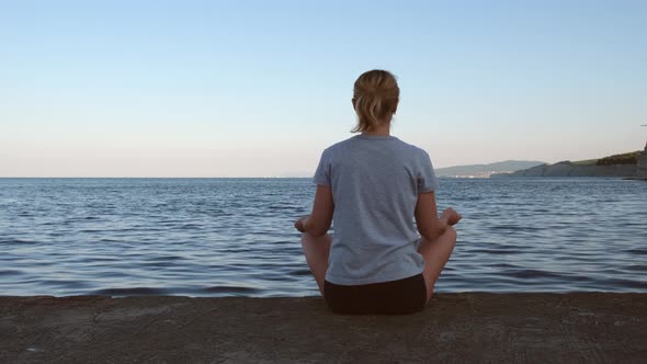 Young Woman Sits in a Lotus Position on the Pier and Looks at the Sea Dawn of the Sun
