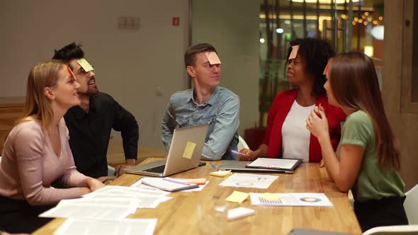 Multiethnic Cheerful Coworkers Playing Guessing Game with Sticky Notes on Forehead After Work for