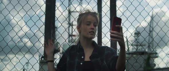 Young woman leaning towards metal fence and takes selfies