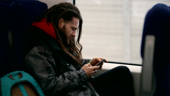 Stylish Man with Long Hair is Riding Train and Surfing Internet By Smartphone with Wifi in Traincar