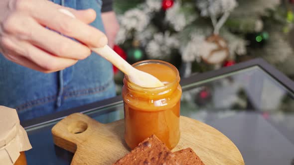 Caramel Appetizingly Flows Down a Spoon Into a Jar on the Background of a Christmas Tree