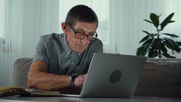 Elderly Senior Man Useing Laptop and Writes Notes in Notebook at Home