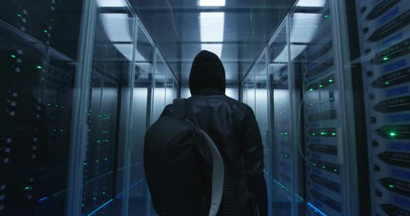 Hacker with a Backpack Walking Through Rows of Rack Servers